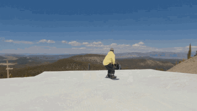 a man in a yellow jacket is riding a snowboard on a snowy slope