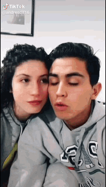 a man and a woman are posing for a picture and the man is wearing a gap hoodie .