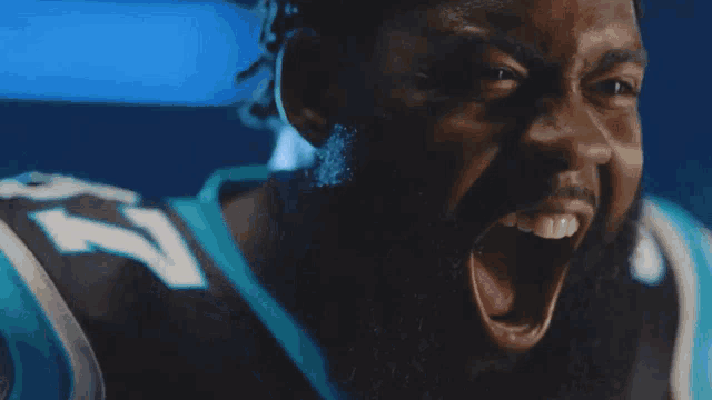 a man with dreadlocks wearing a panthers jersey and gloves