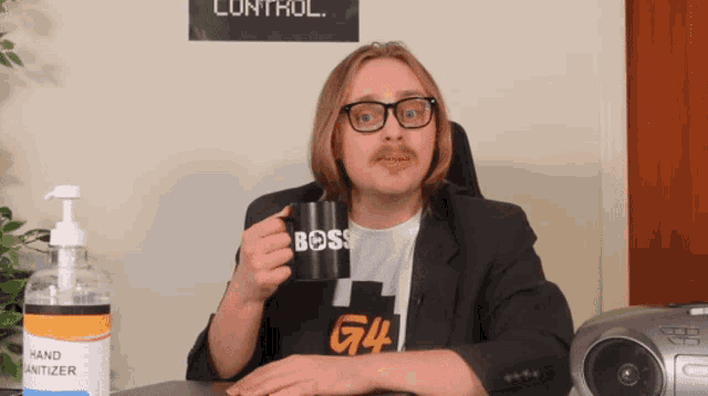 a man sitting at a desk holding a black mug that says boss