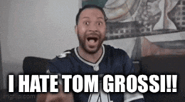 a man is sitting on a couch with his mouth open and says i hate tom grossi .