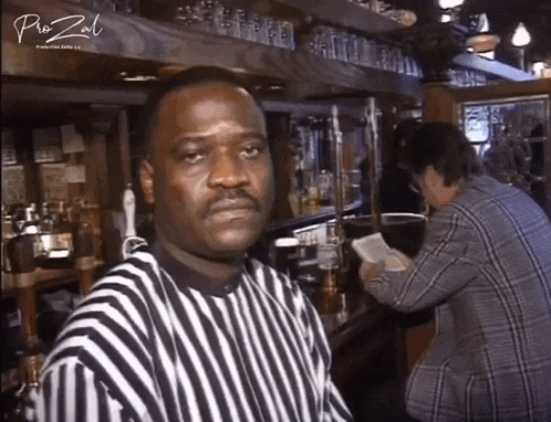 a man in a black and white striped shirt stands in front of a bar with pro zal written on the bottom