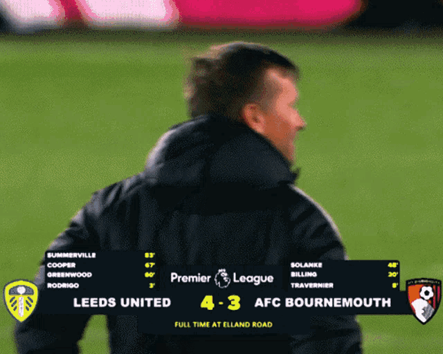 a man stands in front of a scoreboard for a premier league game