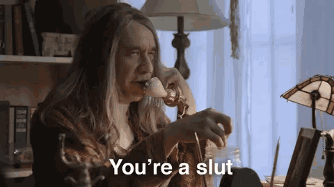 a man with long hair is talking on a telephone and saying you 're a slut .