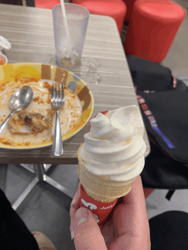a person is holding a jollibee ice cream cone in front of a plate of food