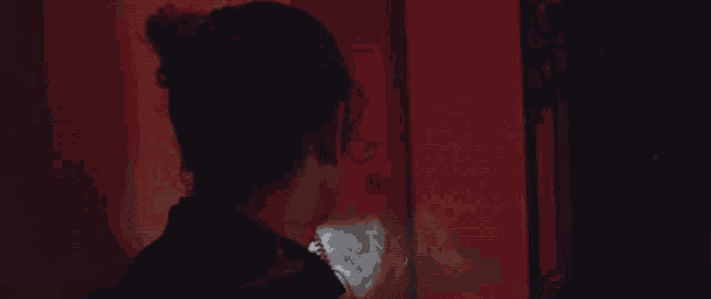 a woman is standing in a dark room with a red wall