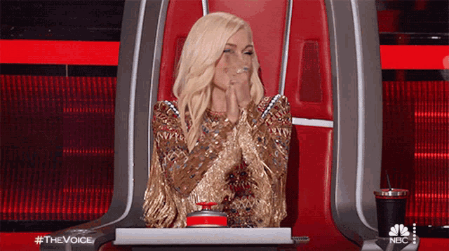 a woman in a gold dress is sitting in a chair with a nbc logo in the background