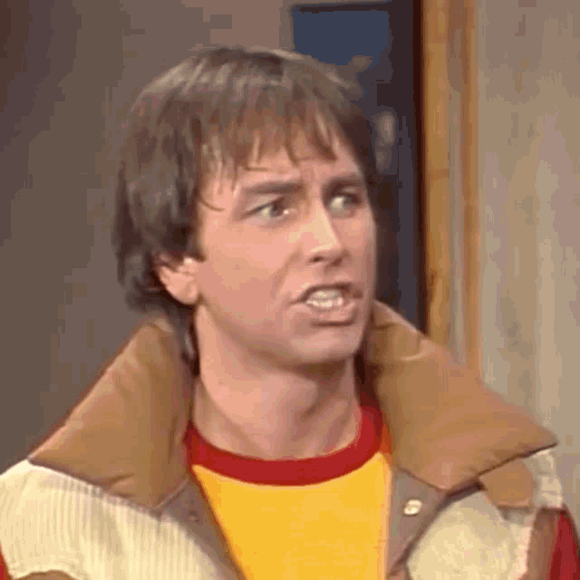 a close up of a man wearing a jacket and a yellow shirt making a funny face .
