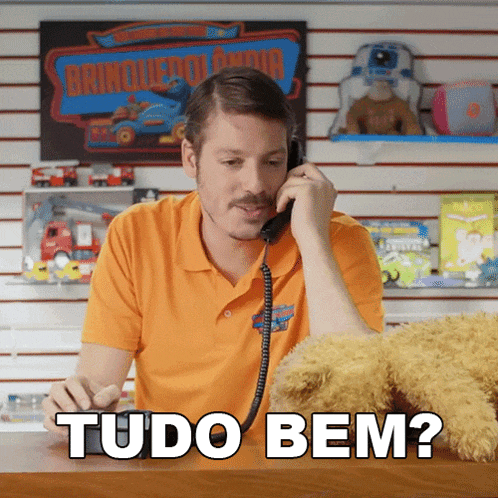 a man in an orange shirt talking on a phone with the words tudo bem written below him