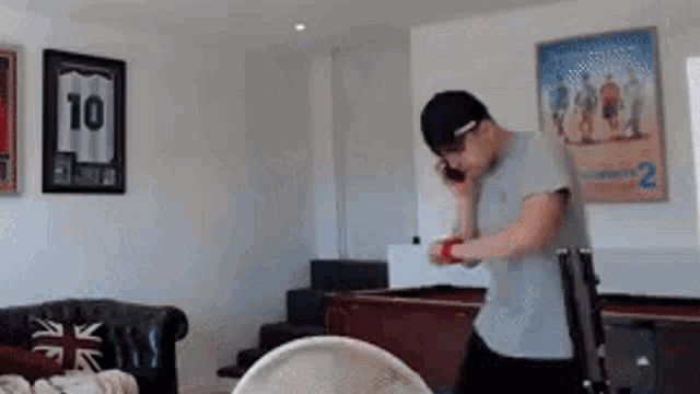 a man is talking on a cell phone in a living room while standing next to a pool table .