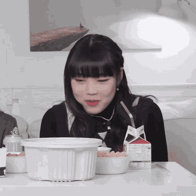 a girl sitting at a table with a carton of milk and a bowl of food