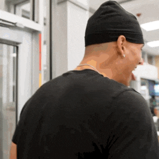 a man wearing a black beanie and a black shirt is standing in front of a glass door