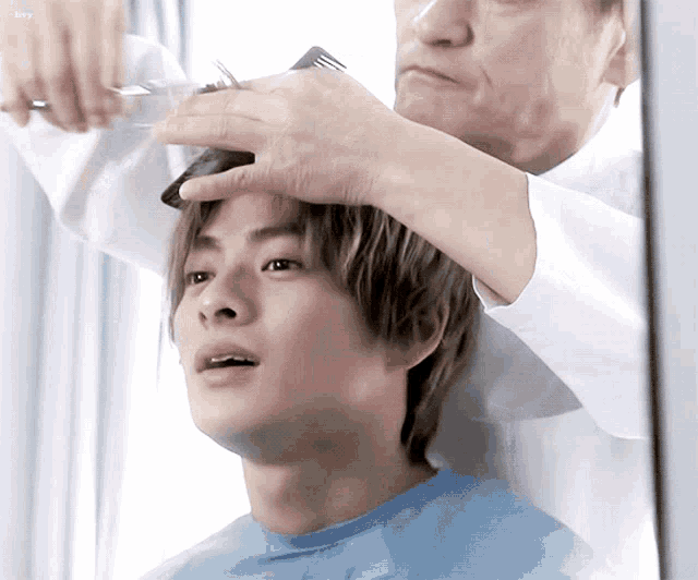 a man in a blue shirt is getting his hair cut by another man