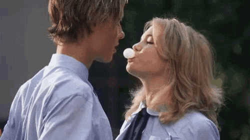 a boy and a girl are blowing a bubble with gum .