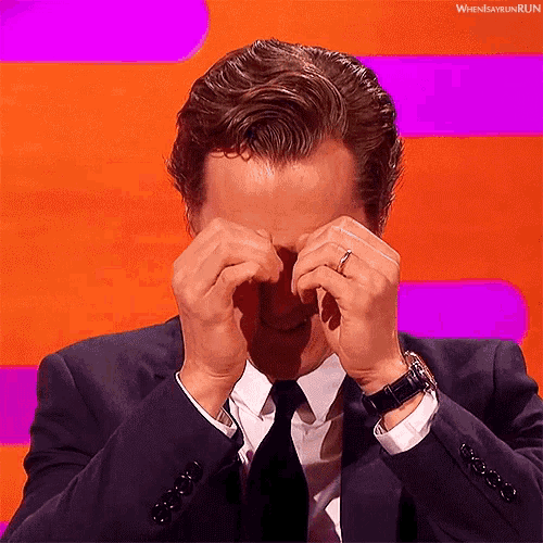 a man in a suit and tie is covering his eyes with his hands while wearing a watch and a ring