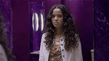 a woman is standing in front of a purple wall and making a funny face .