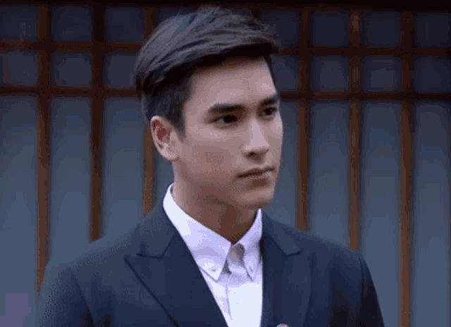 a man in a suit and white shirt is standing in front of a building