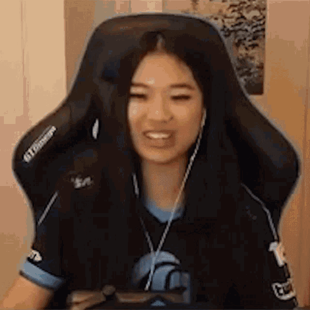 a woman is sitting in a gaming chair wearing headphones and smiling while playing a video game .