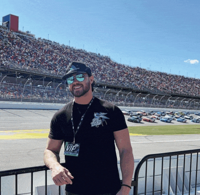 a man wearing sunglasses and a vip tag stands in front of a crowded stadium