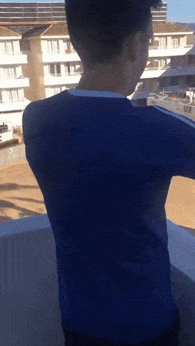 a man in a blue shirt is standing on a balcony looking out over a building