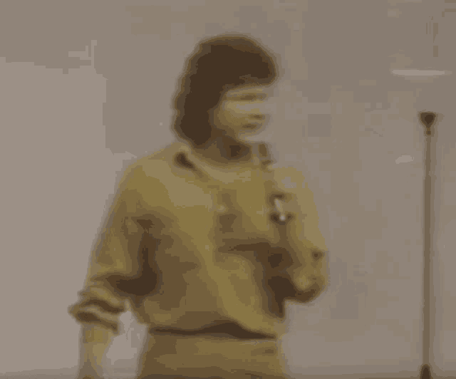 a man in a yellow shirt is standing in front of a microphone in a room .