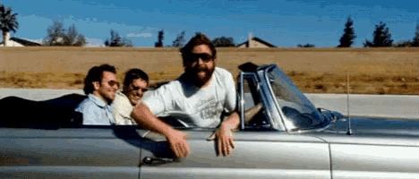 a group of men are riding in a silver convertible car