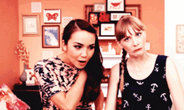two women are standing next to each other in front of a wall with pictures on it