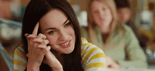 a woman is sitting at a table with her hand on her forehead and smiling .