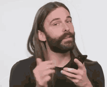 a man with long hair and a beard is using a cell phone .