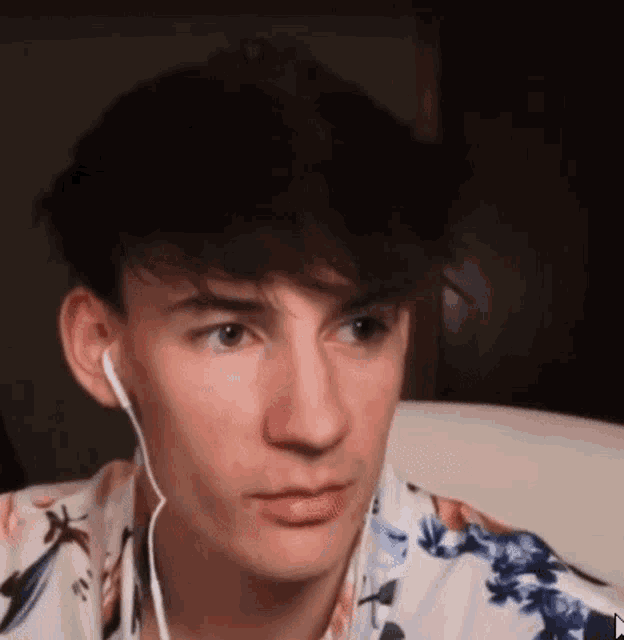 a young man wearing headphones and a floral shirt is sitting on a chair .