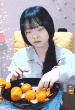 a girl with long black hair is eating oranges from a black bowl