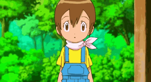 a little girl in overalls and a yellow shirt is standing in front of trees .