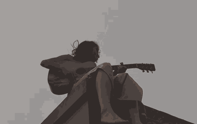 a woman is playing a guitar while sitting on a wall