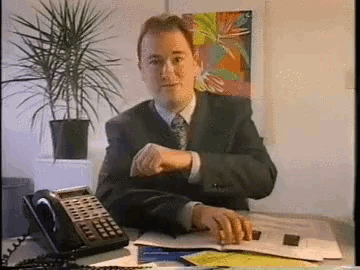 a man in a suit and tie sits at a desk next to a phone