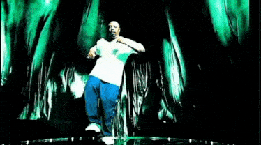a man in a white shirt and blue pants is dancing on a stage in front of a green background .