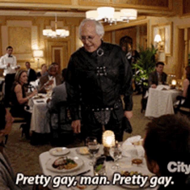 a man is standing in a restaurant talking to a group of people and the caption says pretty gay man pretty gay