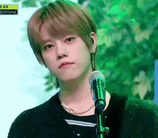a young man is singing into a microphone while wearing a necklace and earrings .