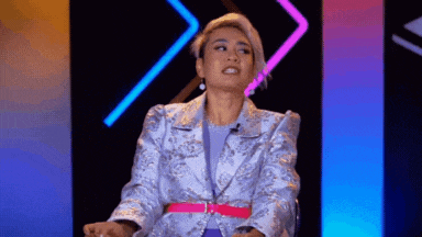 a woman in a purple jacket and pink belt is sitting in front of a colorful background .