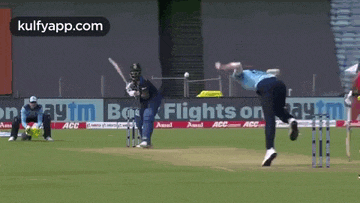 a cricket player is throwing a ball while another player watches