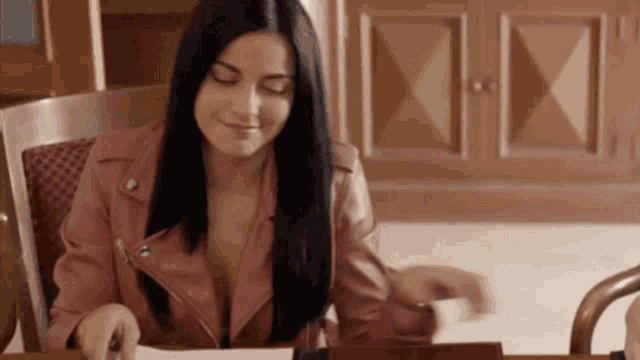 a woman in a pink jacket sits at a desk