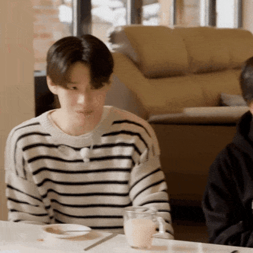 a man in a striped sweater sits at a table with a glass of milk