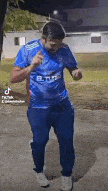 a man wearing a blue shirt and blue pants is dancing in a park .