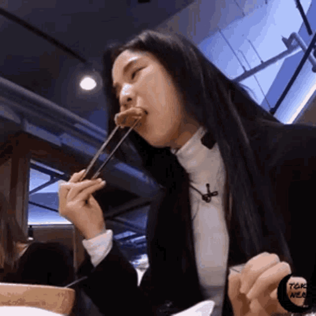 a woman is eating a piece of food with chopsticks and a sticker that says tokyo meal on it