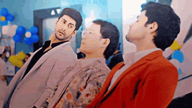 a man in a red jacket is standing next to two other men in suits