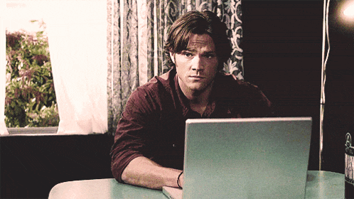 a man sits at a table with a laptop and a bottle of beer on it