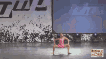 a little girl is dancing on a stage in front of a dance mons sign .