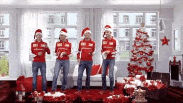 four men wearing santa hats and sweaters that say santander are dancing in a living room