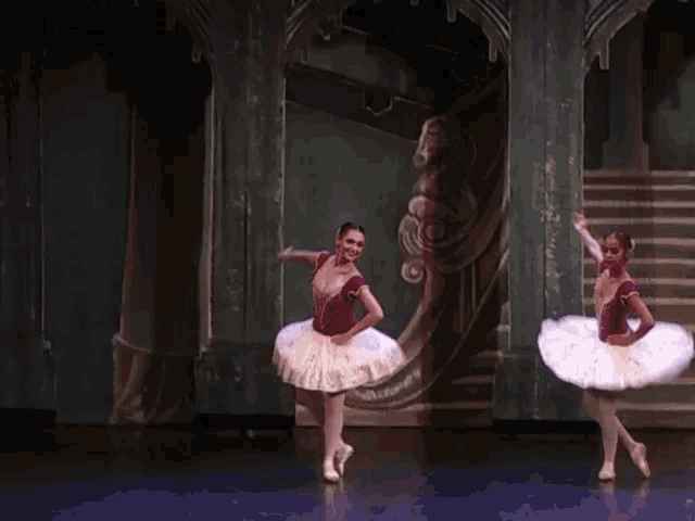 two ballerinas are dancing on a stage in front of a staircase