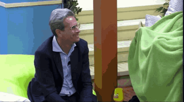 a man in a suit and glasses sits on a green chair