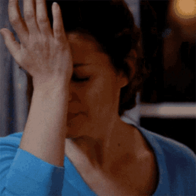 a woman with her hand on her forehead is wearing a blue shirt
